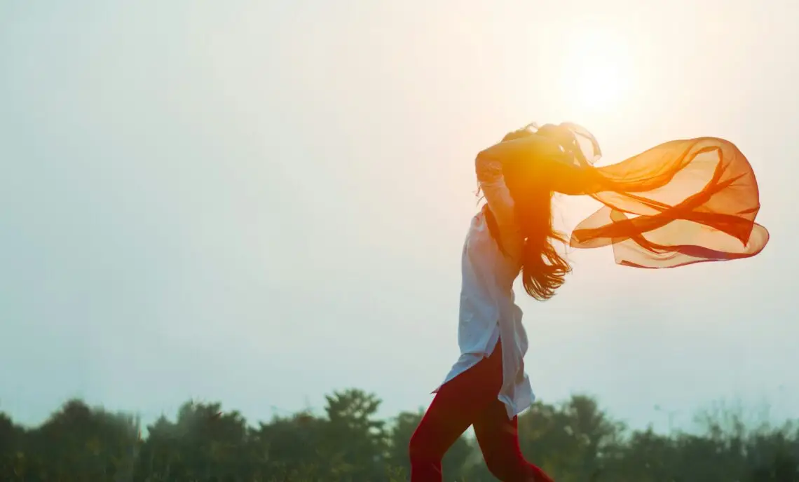 Femme dansant avec un foulard au levier du soleil, symbolisant la liberté et l'acceptation de soi